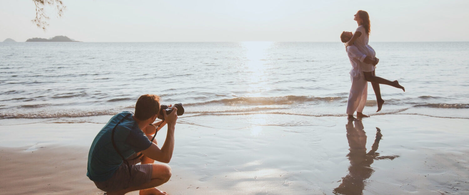 wedding and lifestyle photographer taking photos of affectionate couple on the beach at sunset